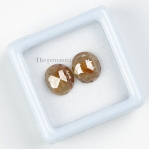 May include: Two brown, faceted, round diamonds in a white box. Thegemsemp is printed on the box.