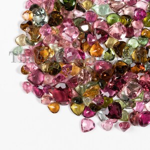 May include: A large collection of pink, green, and brown gemstones. The gemstones are various shapes and sizes, including heart, oval, and pear shapes.