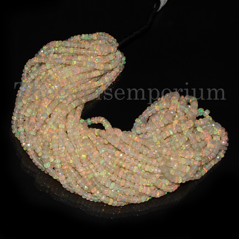 May include: A strand of white opal beads with a rainbow iridescent sheen. The beads are faceted and have a square shape. The strand is approximately 16 inches long.