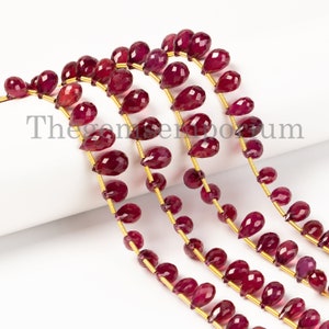 May include: A strand of ruby red gemstone beads in a teardrop shape. The beads are strung on a gold wire and are approximately 10mm in size.