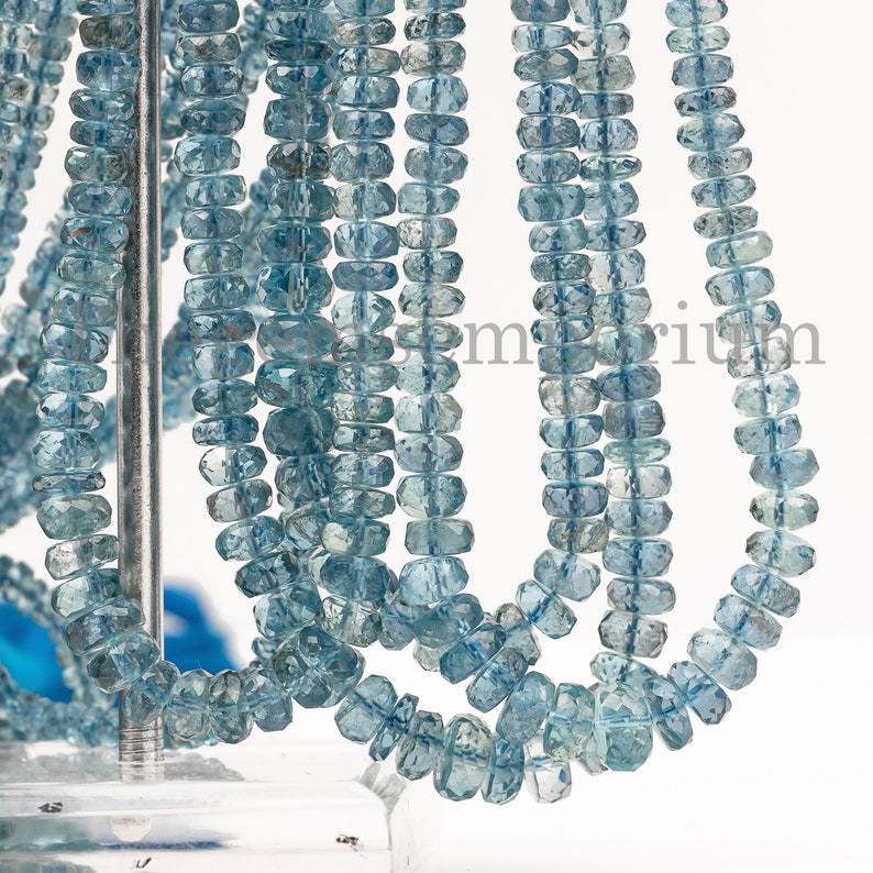 May include: A strand of light blue aquamarine beads, faceted and shaped into rectangular forms. The beads are strung on a wire and are displayed on a white background.