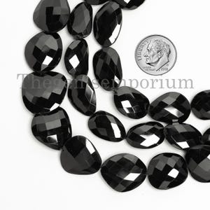 Könnte beinhalten: Eine Kette aus schwarzen facettierten Edelsteinperlen. Die Perlen sind oval geformt und haben eine glatte, polierte Oberfläche. Die Perlen sind auf einem durchsichtigen Faden aufgefädelt und haben einen Durchmesser von etwa 10 mm.