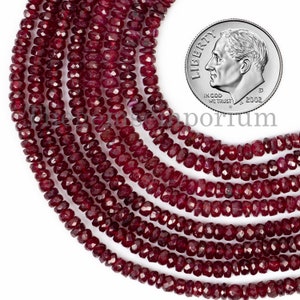 May include: A strand of deep red ruby beads, faceted and round, with a diameter of approximately 4mm. The beads are strung on a clear thread and are shown next to a US dime for scale.