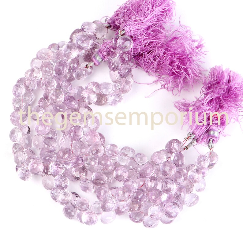May include: Strands of faceted, light purple gemstones with matching lavender tassels. The gemstones are round and have a sparkling, polished appearance. The tassels are made of soft, fluffy material. The image is set against a white background.