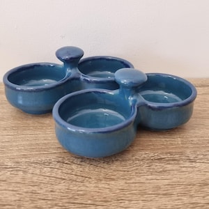 May include: Three blue ceramic serving dishes with a glossy finish. Each dish has two connected compartments and a small handle. The dishes are arranged on a wooden surface.