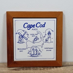 May include: A square tile with a map of Cape Cod, Massachusetts, in blue and white, set in a wooden frame. The map includes illustrations of a windmill, lobster, lighthouse, and sailboat. The words "Cape Cod" and "MASS" are at the top.