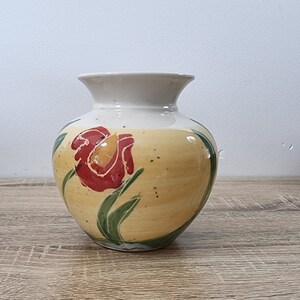 May include: A ceramic vase with a yellow glaze and a red flower design. The vase has a round body and a narrow neck.