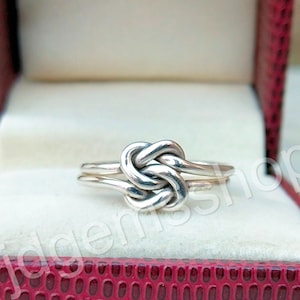 Op de afbeelding: Een zilveren knoop ring met een gepolijste afwerking. De ring zit in een rode fluwelen ringdoos.