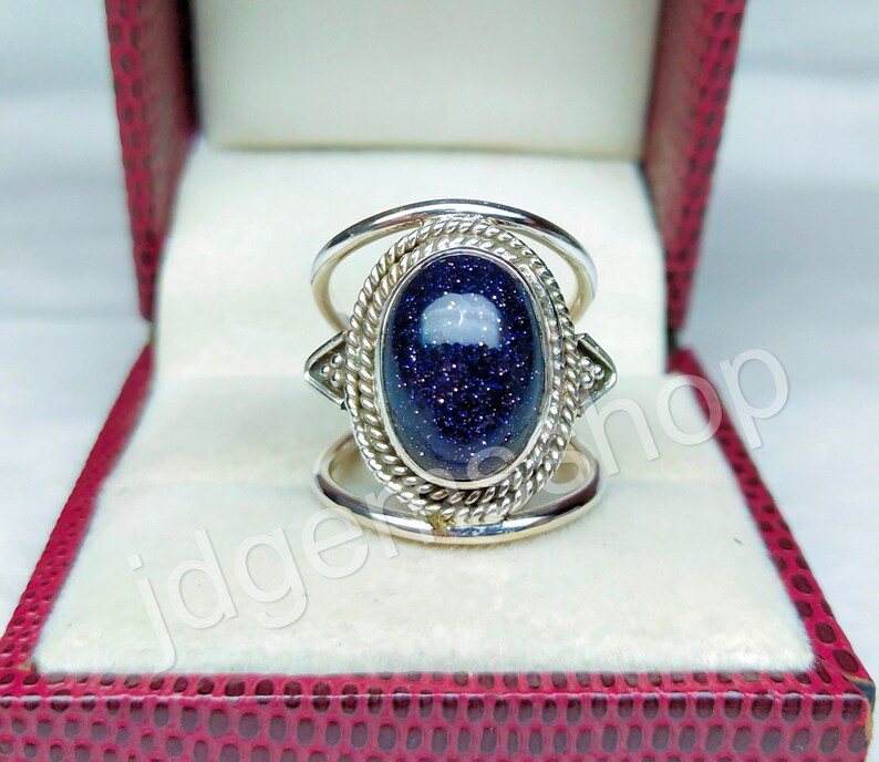May include: A silver ring with a blue gemstone set in a decorative oval bezel. The ring has a double band design with a twisted rope pattern.
