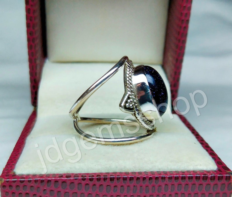 May include: A silver ring with a blue gemstone set in a decorative silver setting. The ring is displayed in a red velvet box.