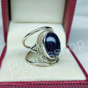 May include: A silver ring with a blue gemstone set in a decorative silver band. The ring is in a red velvet ring box.