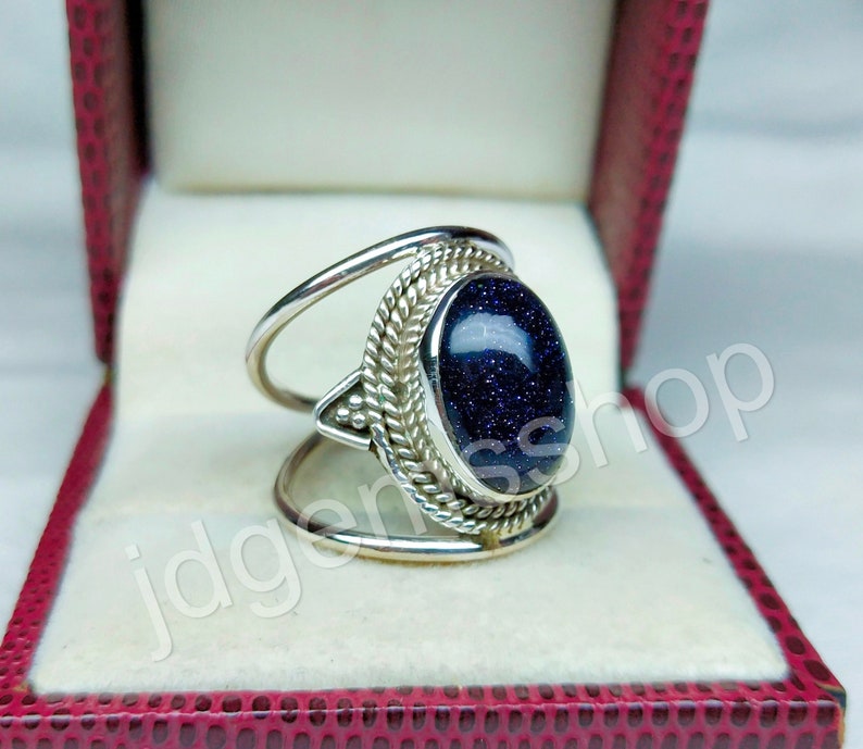 May include: A silver ring with a blue gemstone set in a decorative silver band. The ring is in a red velvet ring box.