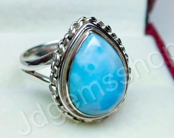 May include: A sterling silver ring featuring a pear-shaped, light blue gemstone. The gemstone is set in a silver bezel with a rope-like border. The ring has a split shank design, adding a unique touch to the jewelry.