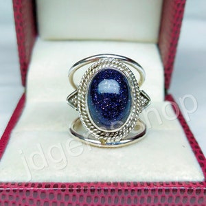 May include: A silver ring with a blue gemstone set in a decorative bezel. The ring has a double band design.