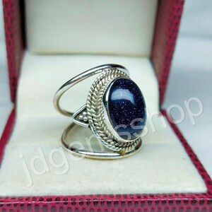 May include: A silver ring with a blue gemstone set in a decorative silver band. The ring is in a red velvet ring box.