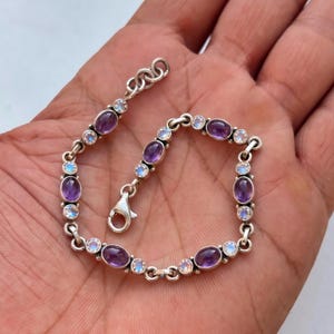 Pode incluir: Pulseira de prata com pedras preciosas ovais de ametista e pedra da lua. A pulseira tem um design de corrente delicada e um fecho de lagosta. As pedras são engastadas em uma moldura de metal prateado.