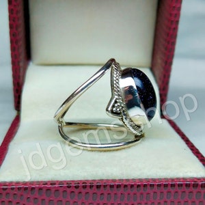 May include: A silver ring with a blue gemstone set in a decorative silver setting. The ring is displayed in a red velvet ring box.