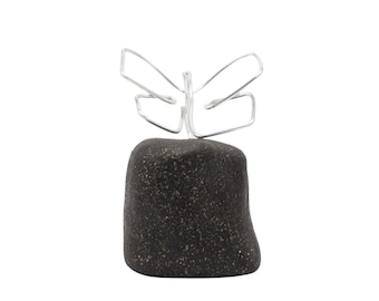 May include: A black stone with a silver wire butterfly sculpture on top. The stone is textured and has a rough surface.