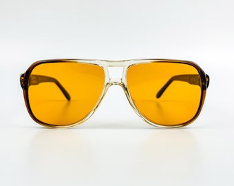 May include: Aviator-style sunglasses with amber-colored lenses. The frames are a combination of clear and brown tortoise shell plastic. The sunglasses have a double bridge and a classic, retro design.