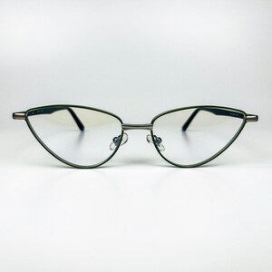 May include: Cat-eye glasses featuring a thin, dark green metal frame with a metallic bridge and temples. The lenses are clear and transparent, and the frame includes adjustable nose pads for a secure fit, showcasing a sleek and pointed silhouette.