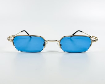 Könnte beinhalten: Sonnenbrille mit goldfarbenem Rahmen und blauen Gläsern. Der Rahmen hat eine dünne, rechteckige Form.