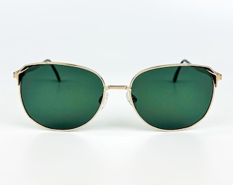 Könnte beinhalten: Sonnenbrille mit goldfarbenem Rahmen und grünen Gläsern. Die Sonnenbrille hat eine runde Form und einen dünnen Goldrahmen. Die Gläser sind einfarbig dunkelgrün, und die Bügel sind dünn und schwarz.