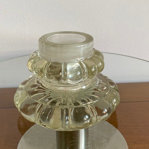 May include: A clear glass candle holder with a textured, fluted design. The holder has a wide base and a narrow opening at the top.
