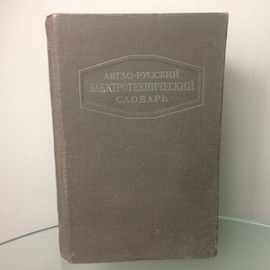 Op de afbeelding: Een bruin boek met de titel "Anglo-Russisch Elektrotechnisch Woordenboek" gedrukt in zilveren letters op de voorzijde.