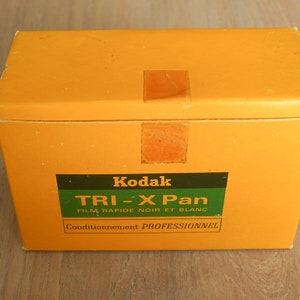 May include: A yellow box with a green label that says "Kodak TRI-X Pan FILM RAPIDE NOIR ET BLANC Conditionnement PROFESSIONNEL."