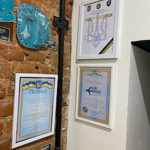 May include: Three framed certificates with blue and yellow accents, featuring the Ukrainian coat of arms and the text "List of Thanks", "Award" and "Award". The certificates are displayed on a brick wall.
