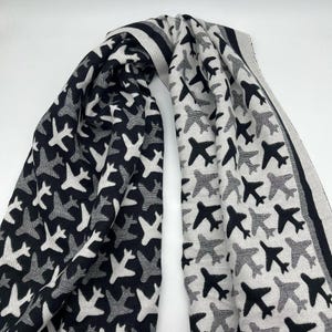 Könnte beinhalten: Ein schwarz-weißer Schal mit einem sich wiederholenden Muster aus Flugzeugen. Der Schal ist aus einem weichen, gewebten Stoff.