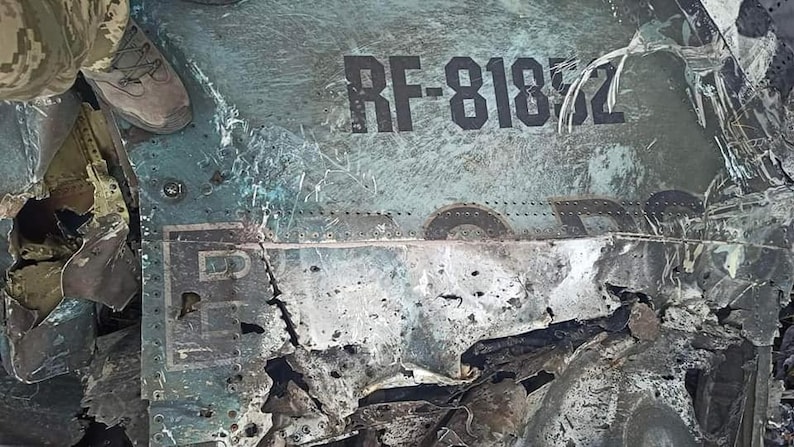May include: Close-up of a damaged aircraft fuselage with the registration number "RF-81872" visible. The metal is heavily damaged and charred, with visible holes and cracks.