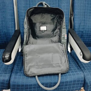 Puede incluir: Una mochila gris con un bolsillo frontal con cremallera y una cremallera negra. La mochila est&aacute; abierta y el interior es visible. La mochila est&aacute; sentada en un asiento con estampado azul y blanco.