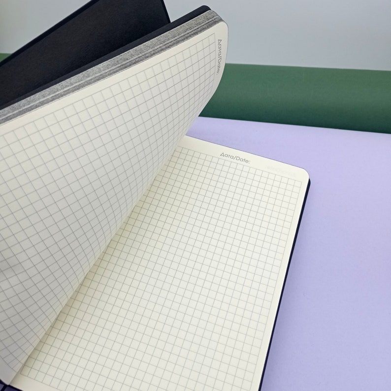 May include: A black and white gridded notebook with a black cover. The notebook is open to a blank page with the words "Data/Date" printed at the top.