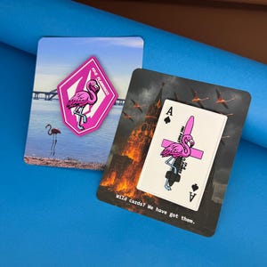 May include: Two rectangular backing cards featuring enamel pins. One card shows a pink flamingo on a diamond-shaped pin with the text FP-5 FLAMINGO. The other card displays an Ace of Spades playing card pin with a flamingo and the text FIRE POINT.