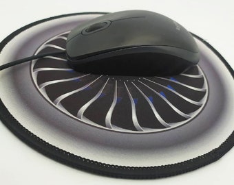 May include: A round black mouse mat with a jet engine design. The mouse mat has a black border and a white background with a grey jet engine design. A black computer mouse is sitting on the mouse mat.