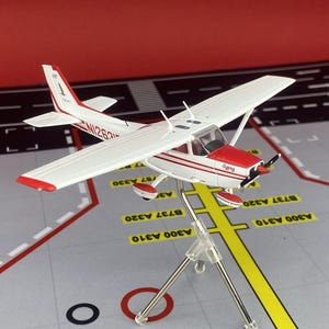 Könnte beinhalten: Ein weiß-rotes Modellflugzeug auf einem silbernen Metallständer. Das Flugzeug hat eine Hochdecker-Konstruktion, einen Propeller an der Nase und die Registrierungsnummer N1263Y am Heck. Das Wort Gypsy ist auf der Flugzeugnase zu sehen.