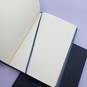 May include: A blue notebook with a grid pattern on the pages. The notebook has a blue ribbon bookmark and the words "Auto/Date" printed on the top of the page.