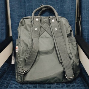 Puede incluir: Una mochila de lona gris con correas ajustables y un asa superior. La mochila tiene un peque&ntilde;o parche con el texto "SA 39" en la parte delantera.