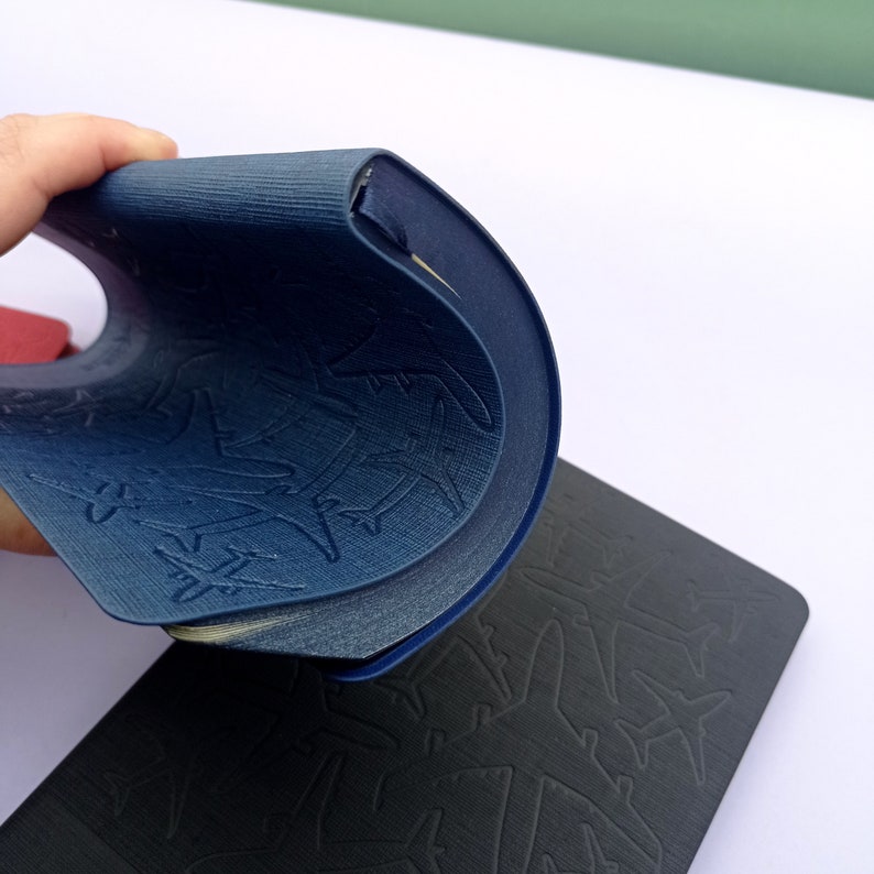 May include: Two notebooks with embossed airplane designs. The top notebook is blue and the bottom notebook is black.