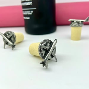 May include: Three silver bottle stoppers with airplane designs. The stoppers are made of metal and have a cork base.