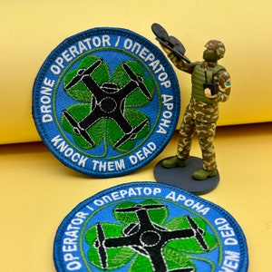 May include: Two embroidered patches with the text "DRONE OPERATOR / ОПЕРАТОР ДРОНА" and "KNOCK THEM DEAD" around a drone design. A miniature figurine of a soldier in camouflage gear is holding a drone controller.