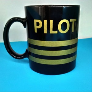 May include: Black ceramic mug with gold lettering that says "PILOT" and three gold stripes.