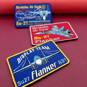 May include: Three embroidered patches featuring the Ukrainian Air Force and Su-27 Flanker aircraft. The patches are rectangular, with blue, red, and yellow backgrounds. Text includes "Ukrainian Air Force," "Su-27," and "Flanker."