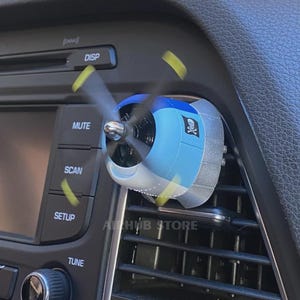 Op de afbeelding: Een blauw-witte vliegtuigpropeller-autoluchtverfrisser bevestigd aan een ventilatierooster van het dashboard. De propeller heeft gele uiteinden en is in beweging. Een klein zwart-wit doodskop-embleem is gedrukt op de zijkant van de blauwe motorkap.