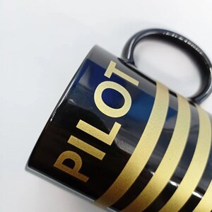 May include: Black ceramic mug with gold stripes and the word "PILOT" in gold lettering.