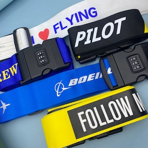 Op de afbeelding: Vijf bagagelussen met verschillende ontwerpen en kleuren. De lussen hebben een cijferslot en de tekst "I ♥ FLYING", "PILOT", "BOEING", "CREW" en "FOLLOW ME".