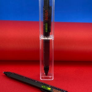 Könnte beinhalten: Ein schwarzer Multifunktions-Stift mit Wasserwaage, Lineal und Stift. Der Stift befindet sich in einem durchsichtigen Kunststoffetui und trägt den Schriftzug "NASA" in Rot.