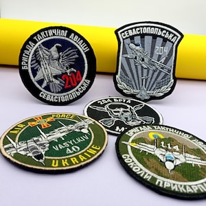 Op de afbeelding: Een verzameling geborduurde patches met militaire luchtvaartthema's. De patches tonen vliegtuigafbeeldingen en tekst, waaronder "Air Force" en "Ukraine". Ze hebben verschillende vormen, met kleuren als groen, zwart en blauw. Afmetingen zijn niet van toepassing.