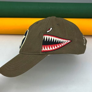 May include: A green baseball cap with a red and white shark tooth graphic and the word "CURT" embroidered on the side.